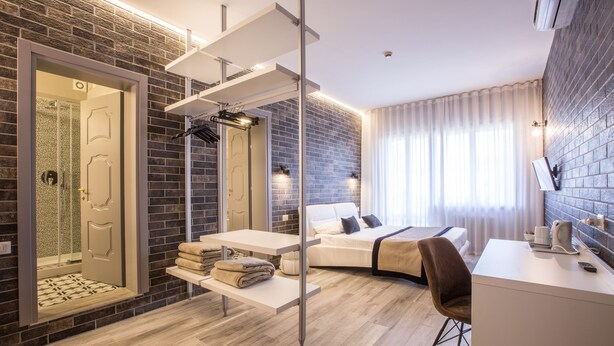 A modern hotel room with a brick wall, a bed, a desk, and a shower area. - Hotel Ariston (Mestre)
