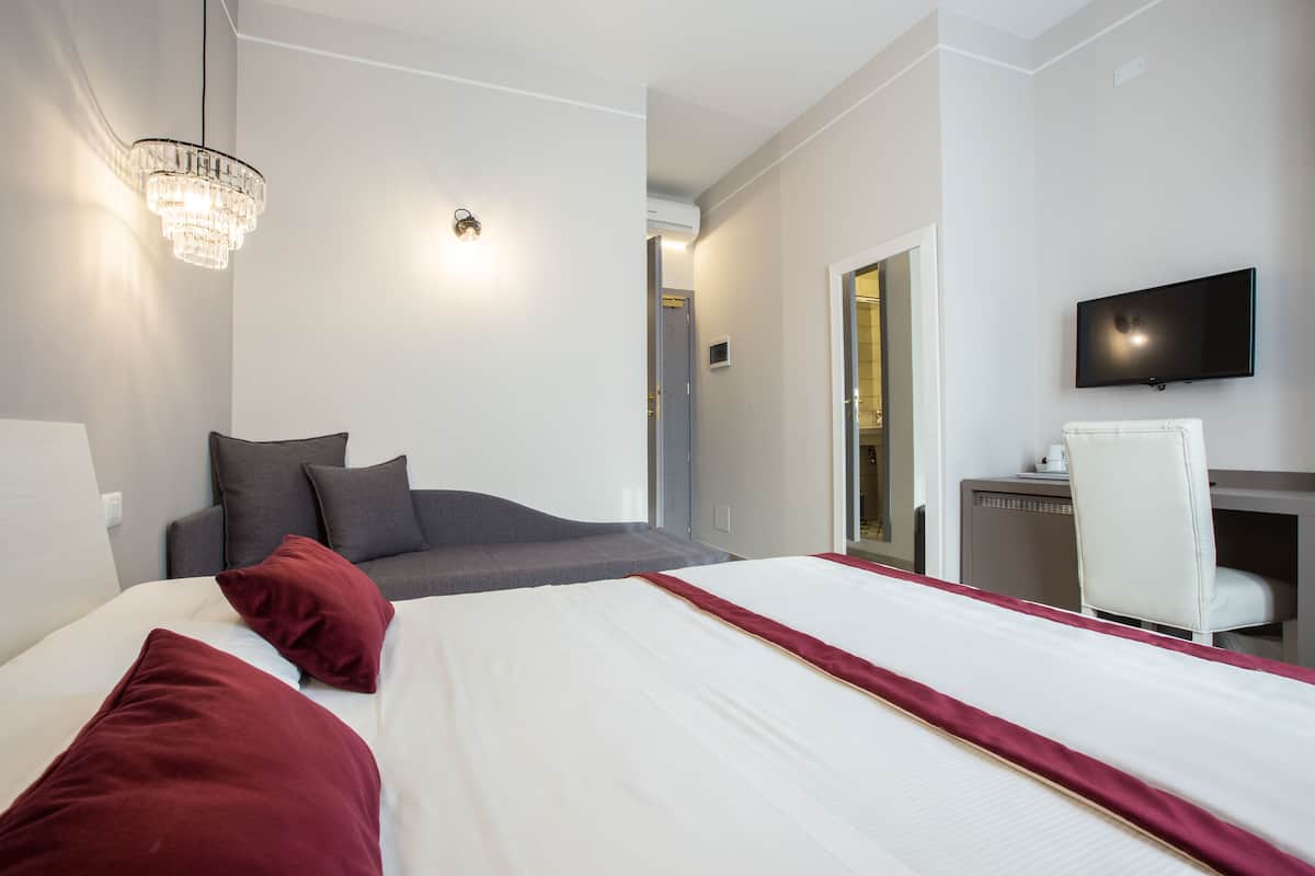 A hotel room with a bed, a desk, a chair, a television, and a chandelier.