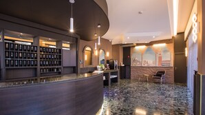 A modern hotel lobby with a curved reception desk, a display of framed items, and a seating area with a view of a cityscape mural. - Hotel Ariston (Mestre)