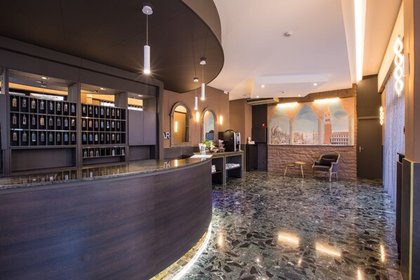 A modern hotel lobby with a curved reception desk, a display of framed items, and a seating area with a view of a cityscape mural. - Hotel Ariston (Mestre)