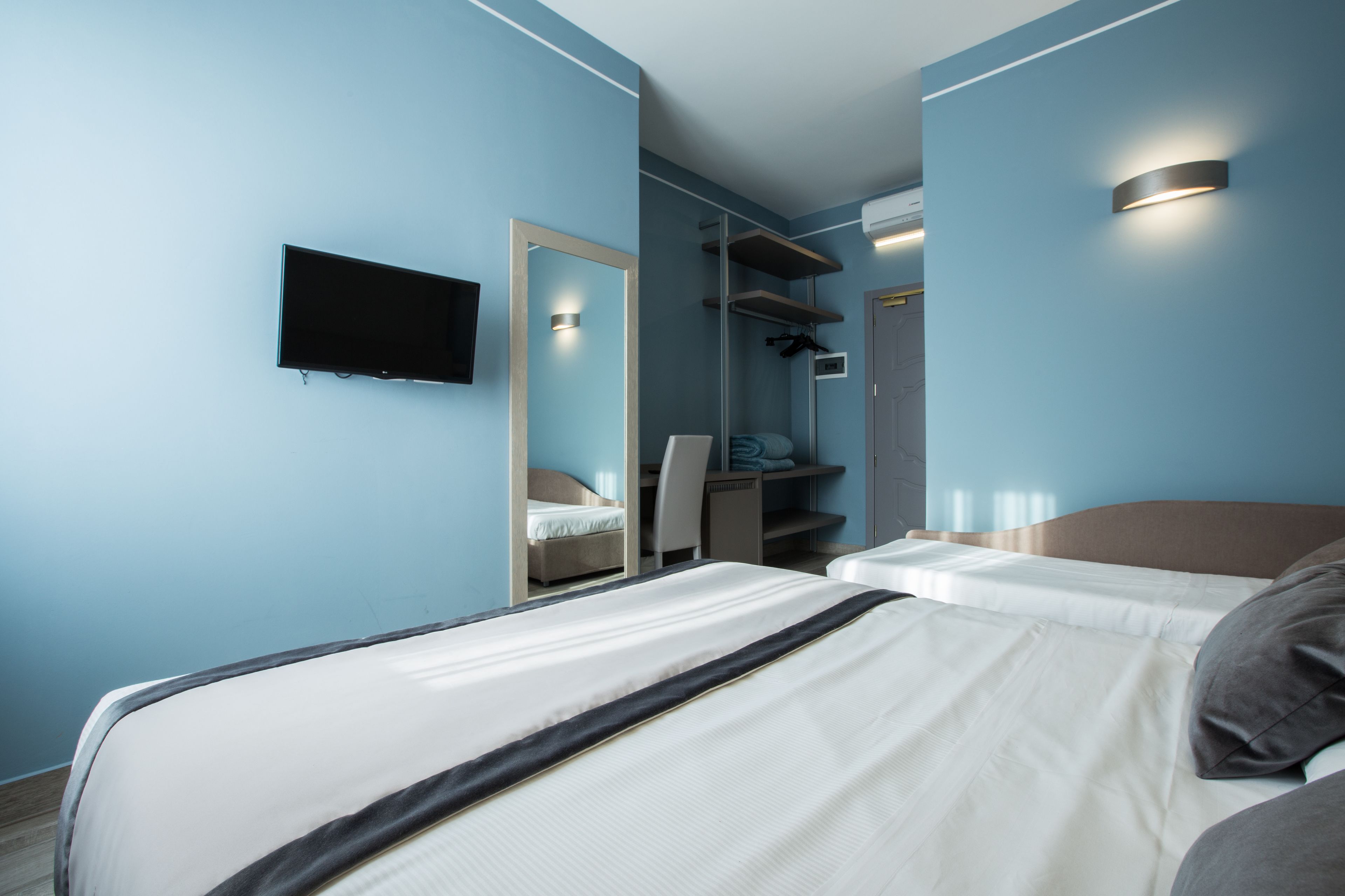 A hotel room with two beds, a TV mounted on the wall, a desk, and a wardrobe.