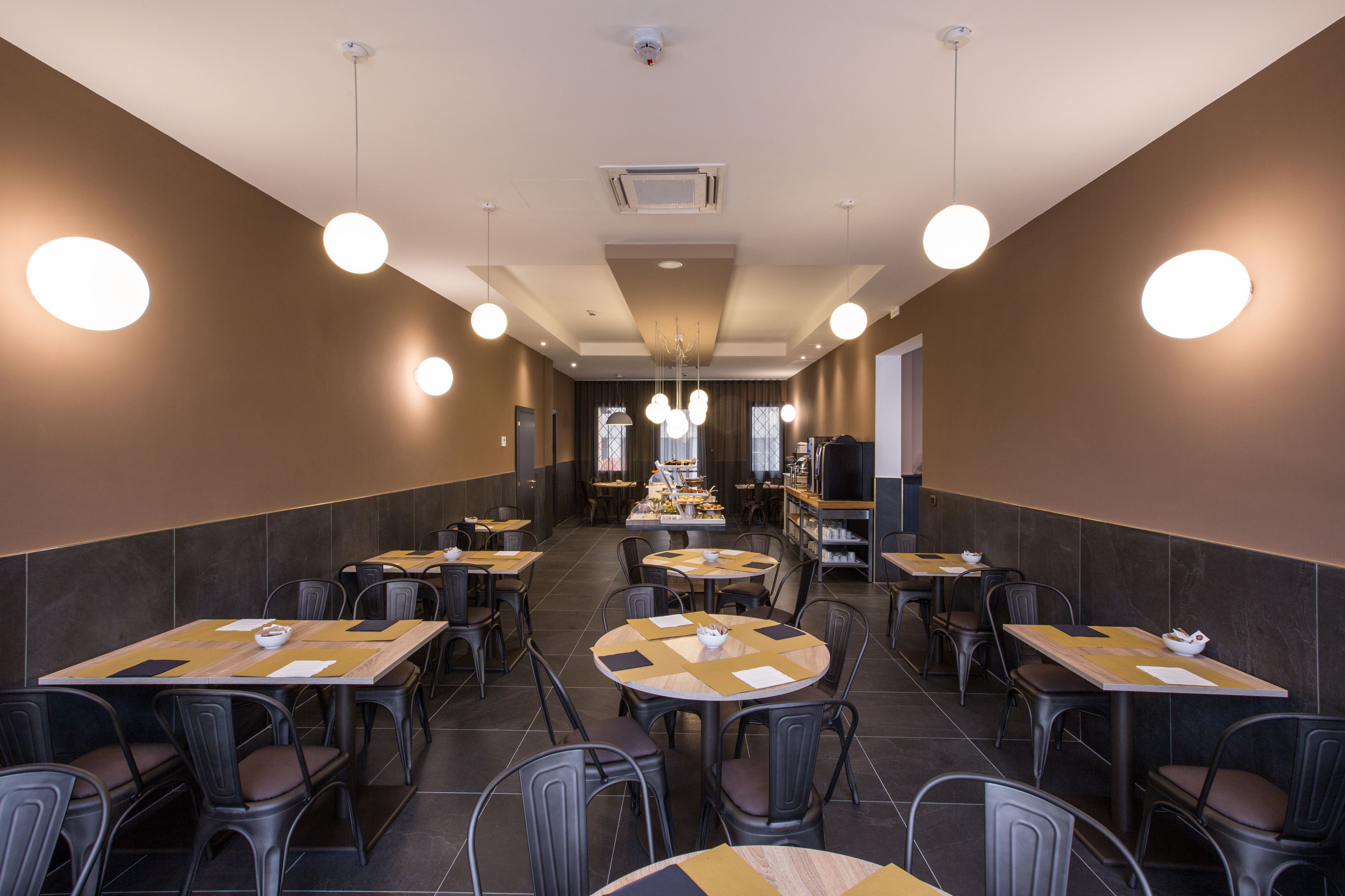 A restaurant with multiple tables and chairs, arranged in a spacious layout with hanging lights.