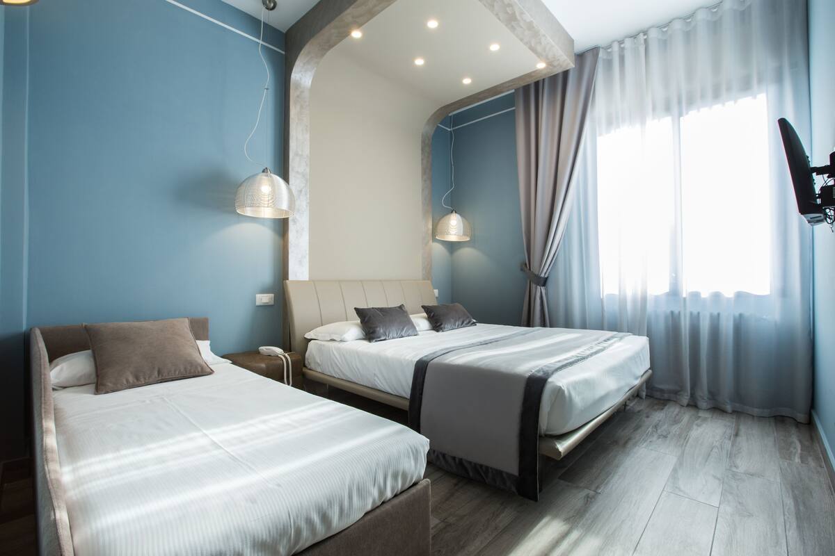 A hotel room with two beds, a large window with curtains, and a mounted TV.
