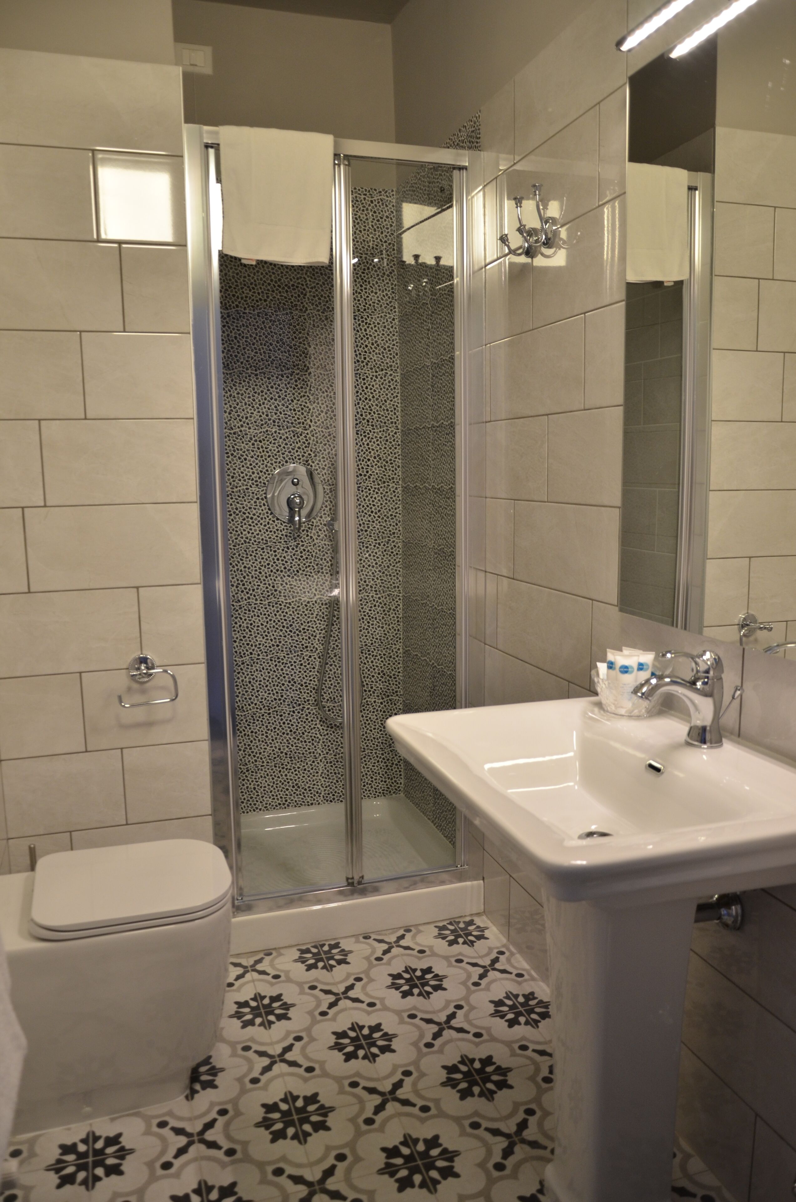 Un baño con cabina de ducha de vidrio, un lavabo blanco y baldosas de suelo con diseño.