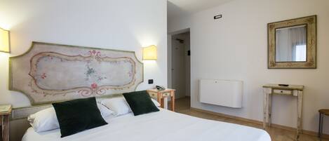A hotel room with a large bed, a bedside table with a lamp, a small table with a mirror, and a radiator on the wall.
