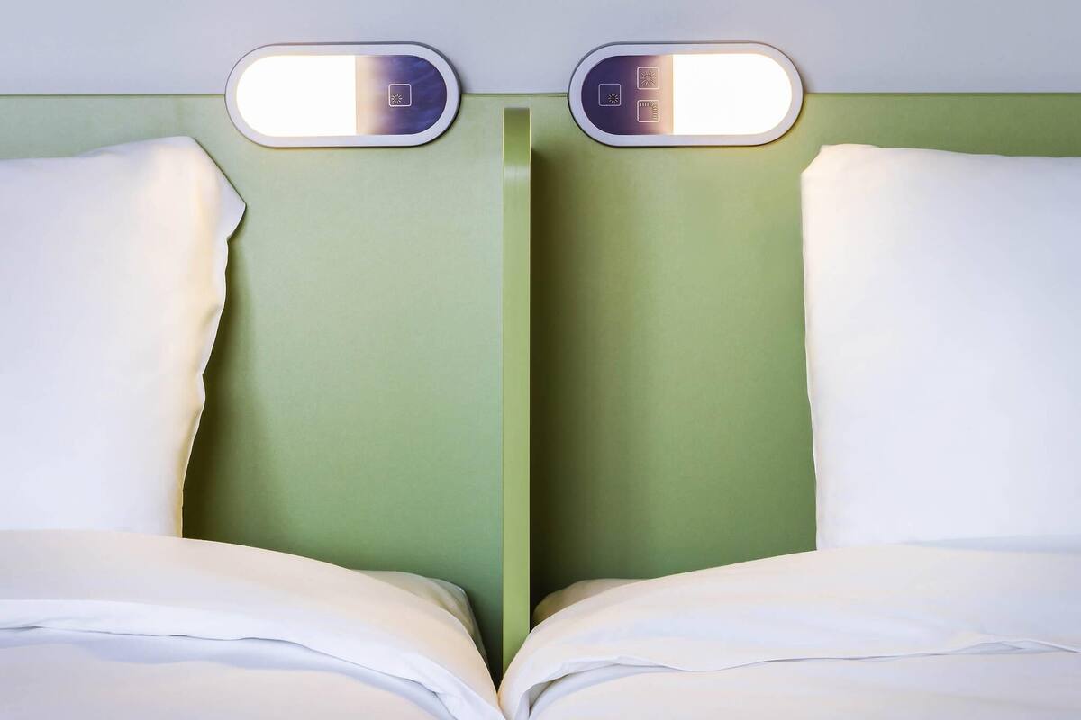 A room with two beds, each with a headboard and a light fixture above.