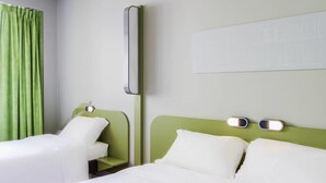 A hotel room with two beds, a green headboard, a bedside table with a lamp, and a wall-mounted light. - ibis budget Braga Centro (Braga)