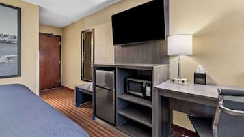 A hotel room with a bed, a desk with a microwave, a refrigerator, a TV, and a chair.