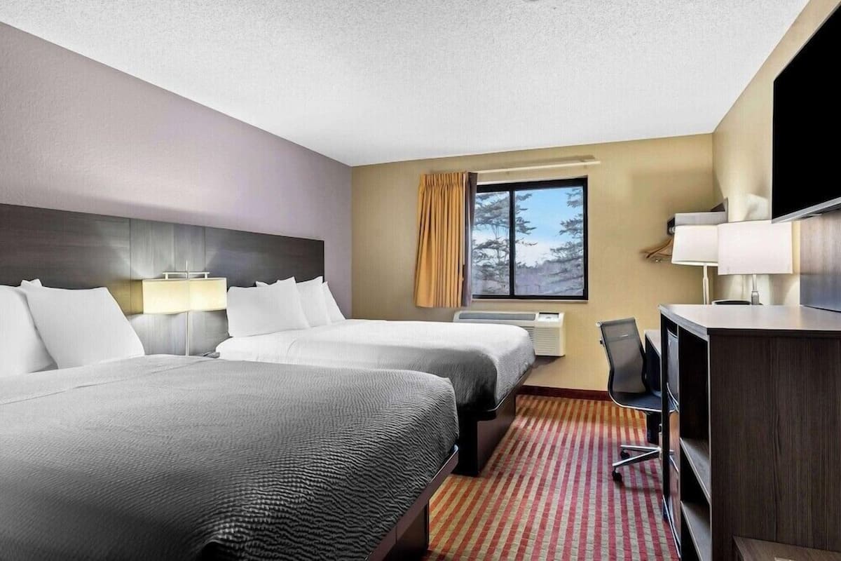 Een hotelkamer met twee bedden, een bureau met stoel, een televisie en een raam met gordijnen.