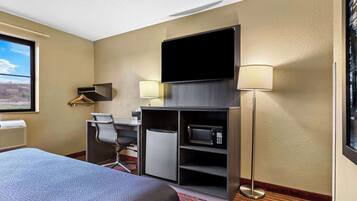 A hotel room with a bed, desk, chair, television, and microwave.