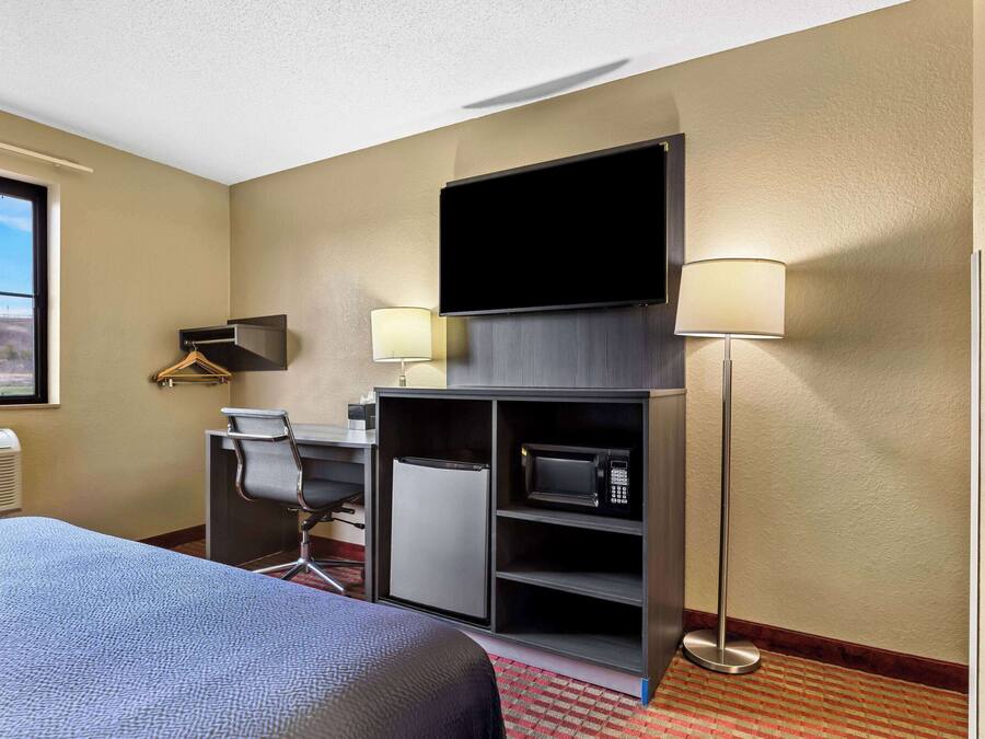 A hotel room with a bed, desk, chair, television, and microwave.