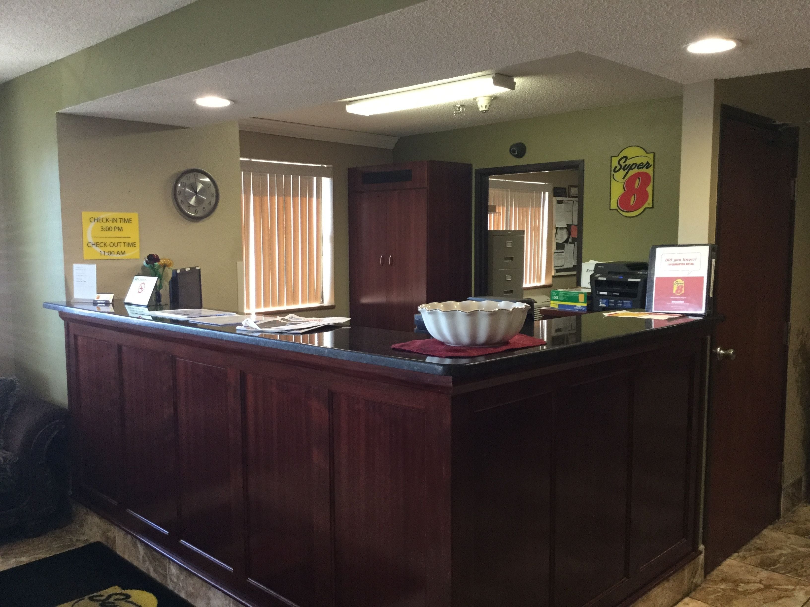 A reception area with a wooden counter, a clock, and a sign indicating check-in and check-out times.