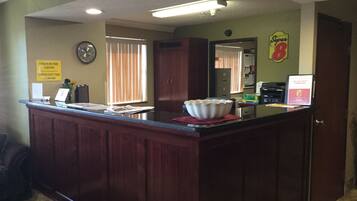 A reception area with a wooden counter, a clock, and a sign indicating check-in and check-out times.