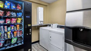 A hotel room with a vending machine stocked with snacks, a washing machine, and a refrigerator.