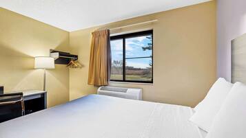 Habitación de hotel con cama, escritorio, lámpara, ventana con cortinas y equipo de aire acondicionado.