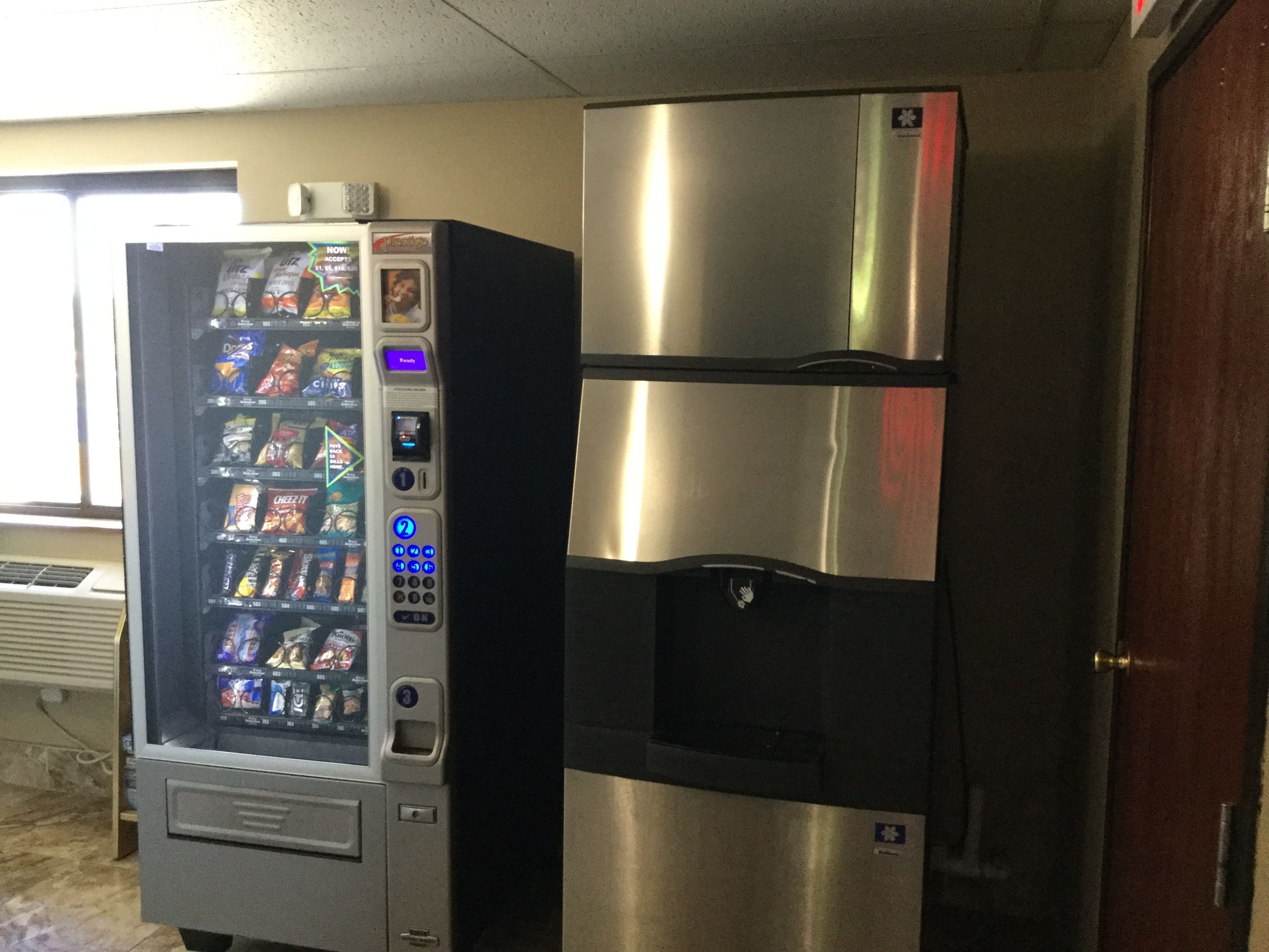 A vending machine and a stainless steel refrigerator in a room.