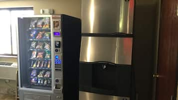 A vending machine and a stainless steel refrigerator in a room.