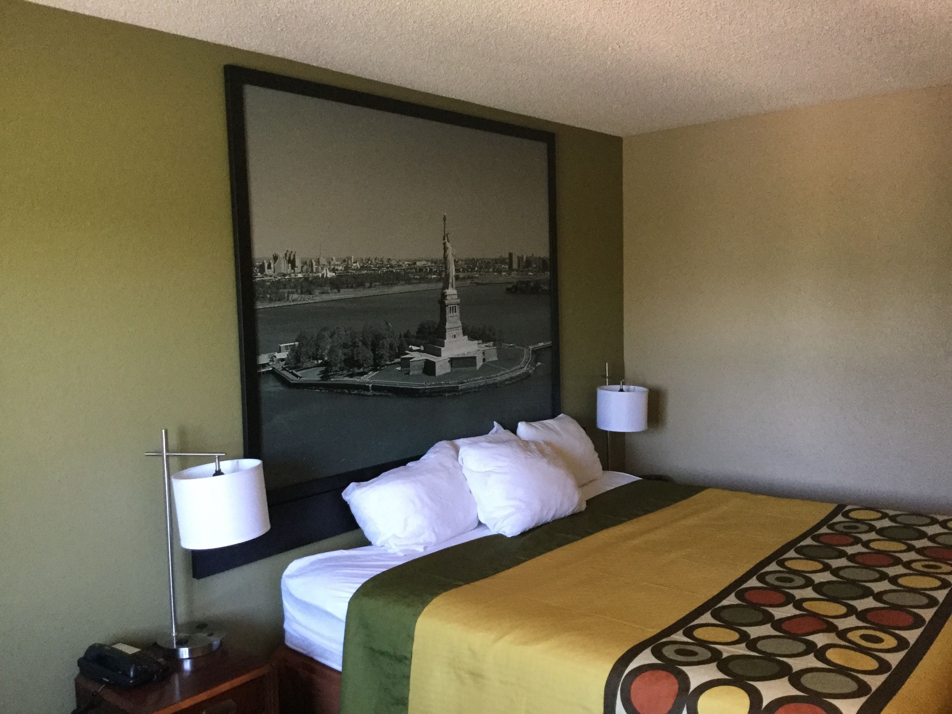 A hotel room with a bed, a nightstand, a lamp, and a framed picture of a cityscape on the wall.