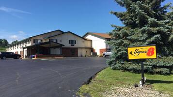 A Super 8 motel with a parking lot, a covered entrance, and a large evergreen tree in front.
