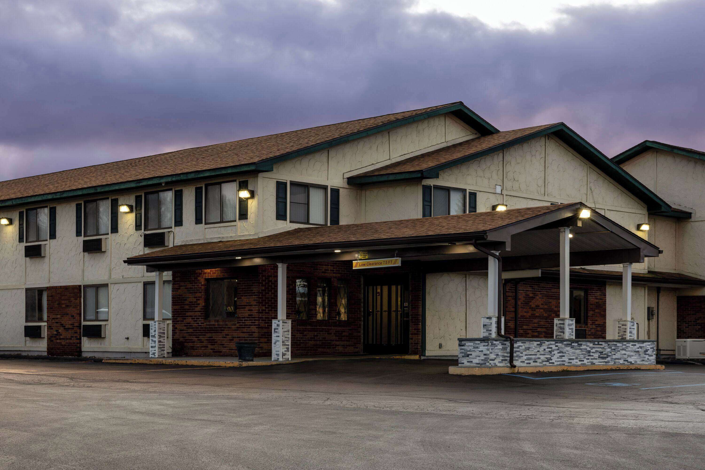 Un hôtel à deux étages, avec une façade en briques, une entrée abritée et un parking.