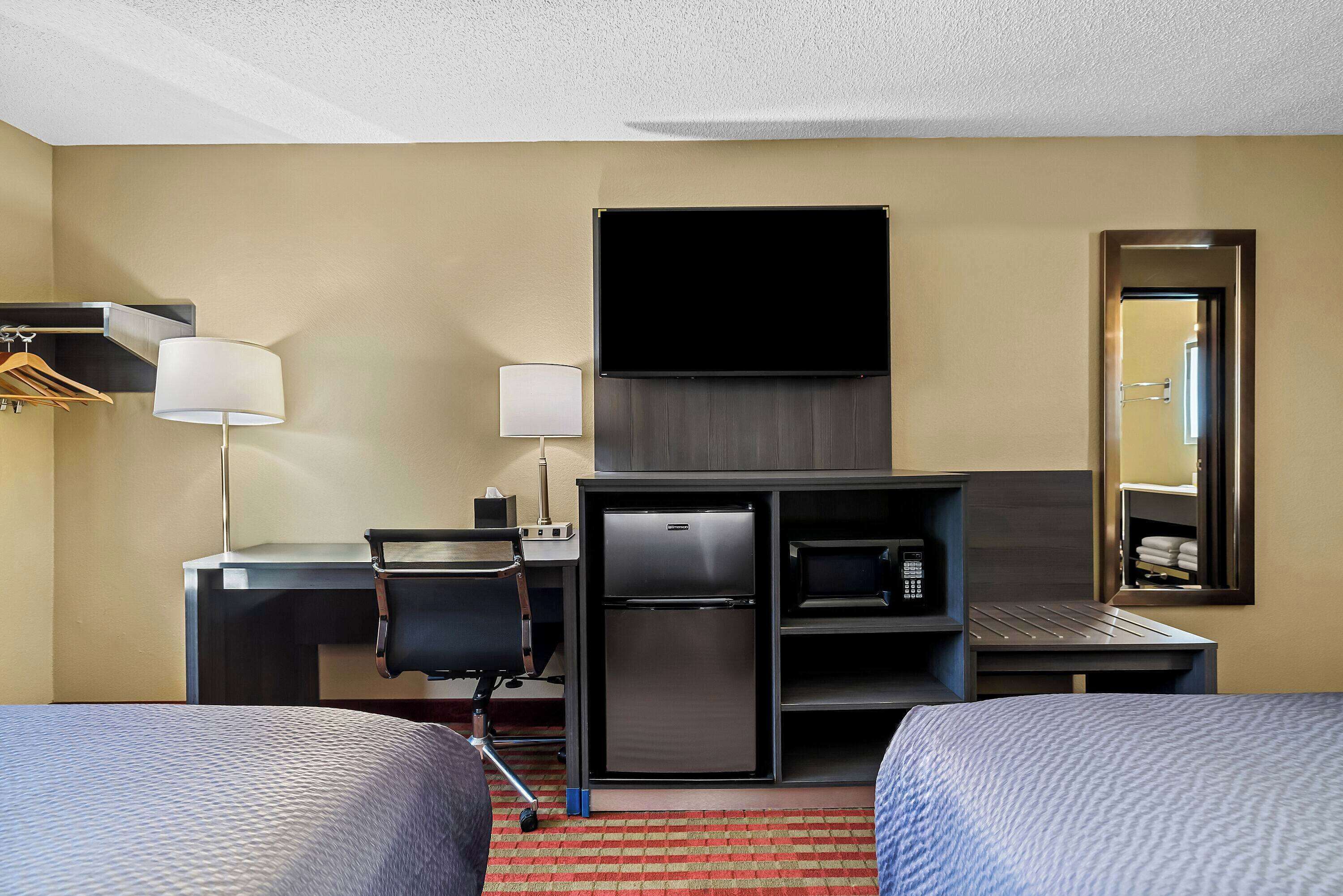 Habitación de hotel con dos camas, un escritorio con computadora, refrigerador, microondas y televisor de pantalla plana.