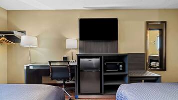 A hotel room with two beds, a desk with a computer, a refrigerator, a microwave, and a flat-screen TV.