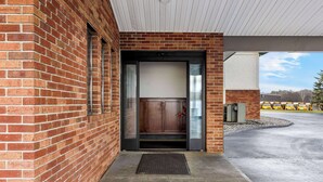 A brick building with a glass door entrance, a metal vent, and a concrete ground.