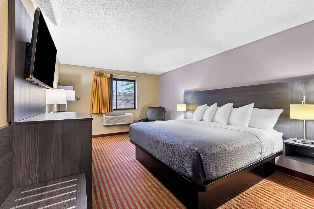 Habitación de hotel con una cama grande, un televisor de pantalla plana en la pared, un escritorio y una ventana con cortinas.