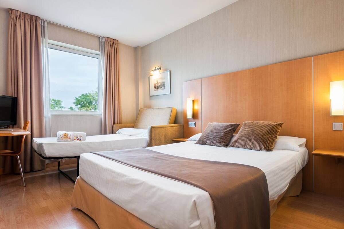 Habitación de hotel con dos camas, un escritorio, una silla, un televisor y una ventana con cortinas.