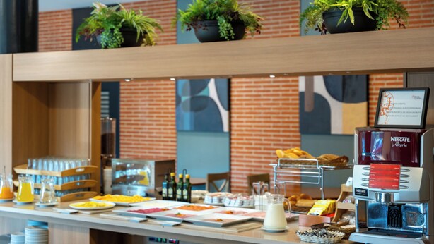Un bufé de desayuno con diversos alimentos, una máquina de café y plantas en macetas sobre estantes.