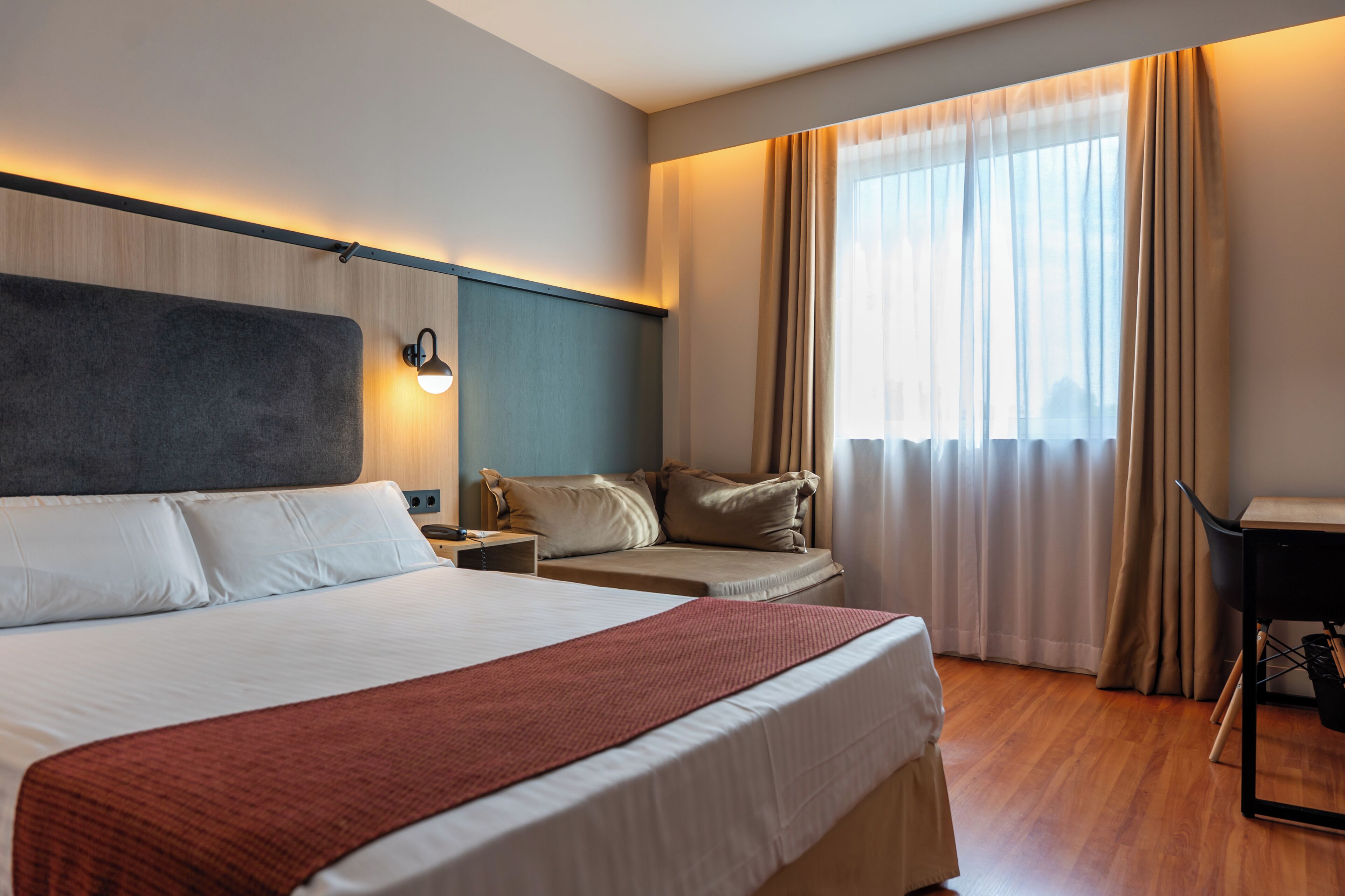 Habitació d'hotel amb un llit gran, escriptori, cadira i finestra amb cortines.