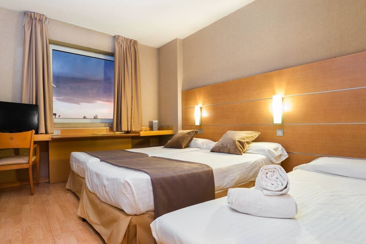 Una habitación de hotel con dos camas, un escritorio, una silla, un televisor y una ventana con cortinas.