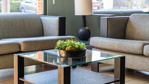 Una sala de estar moderna con una mesa de centro de vidrio, dos sofás grises, una lámpara de pie negra y una planta en maceta.