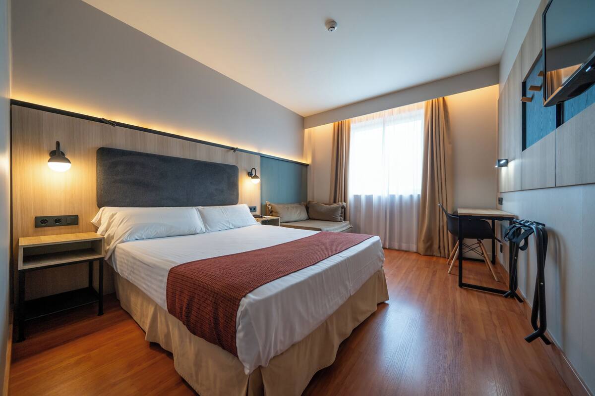 Una habitación de hotel con cama, mesitas de noche, un escritorio y una silla.