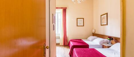 Una habitación de hotel con dos camas, una puerta de madera, un candelabro y una ventana con cortinas.