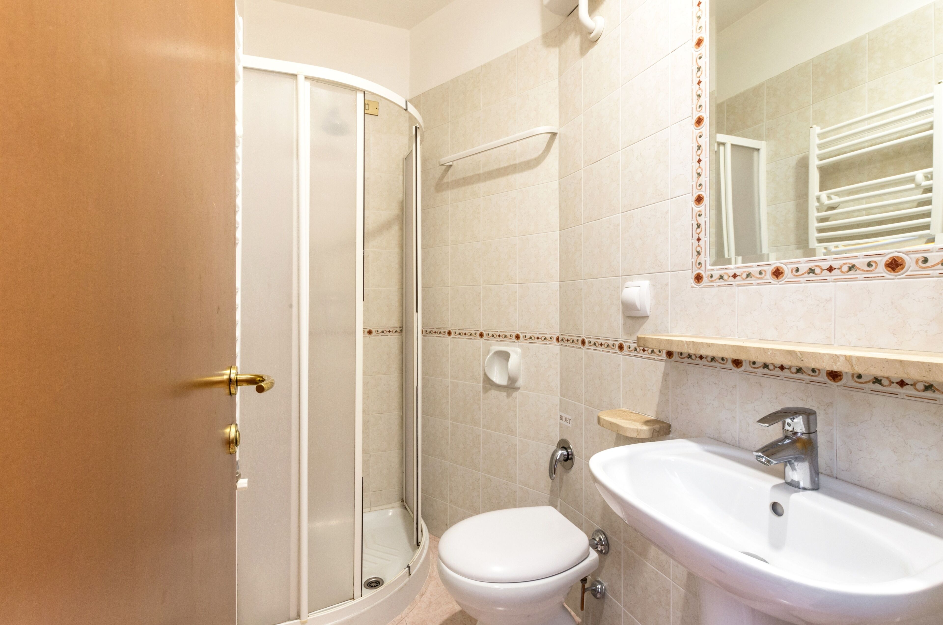 Un baño con ducha, inodoro, lavabo y un espejo con azulejos decorativos.