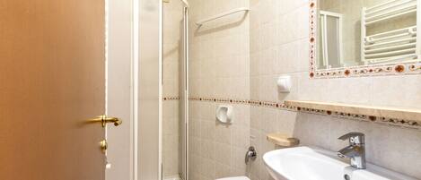 Un baño con ducha, inodoro, lavabo y un espejo con azulejos decorativos.