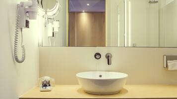 A modern bathroom with a white sink, a handheld hair dryer, a mirror, and a glass-enclosed shower.