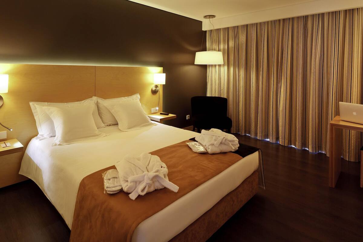 A hotel room with a large bed, a desk, a chair, and a laptop.