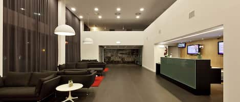 A modern lobby with dark-toned sofas, a reception desk, and a large window with curtains.