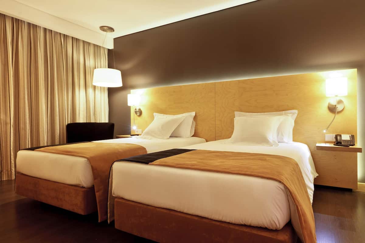 A hotel room with two beds, a chair, a desk with a phone, and a lamp.