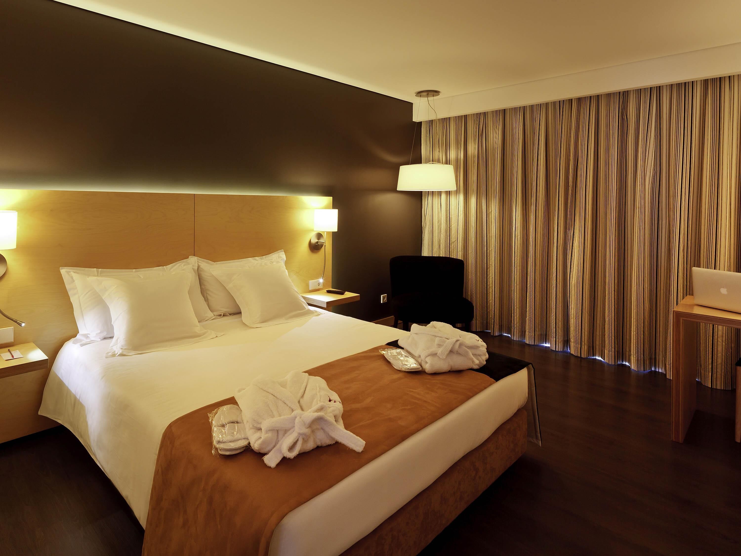 A hotel room with a large bed, a desk, a chair, and a laptop.