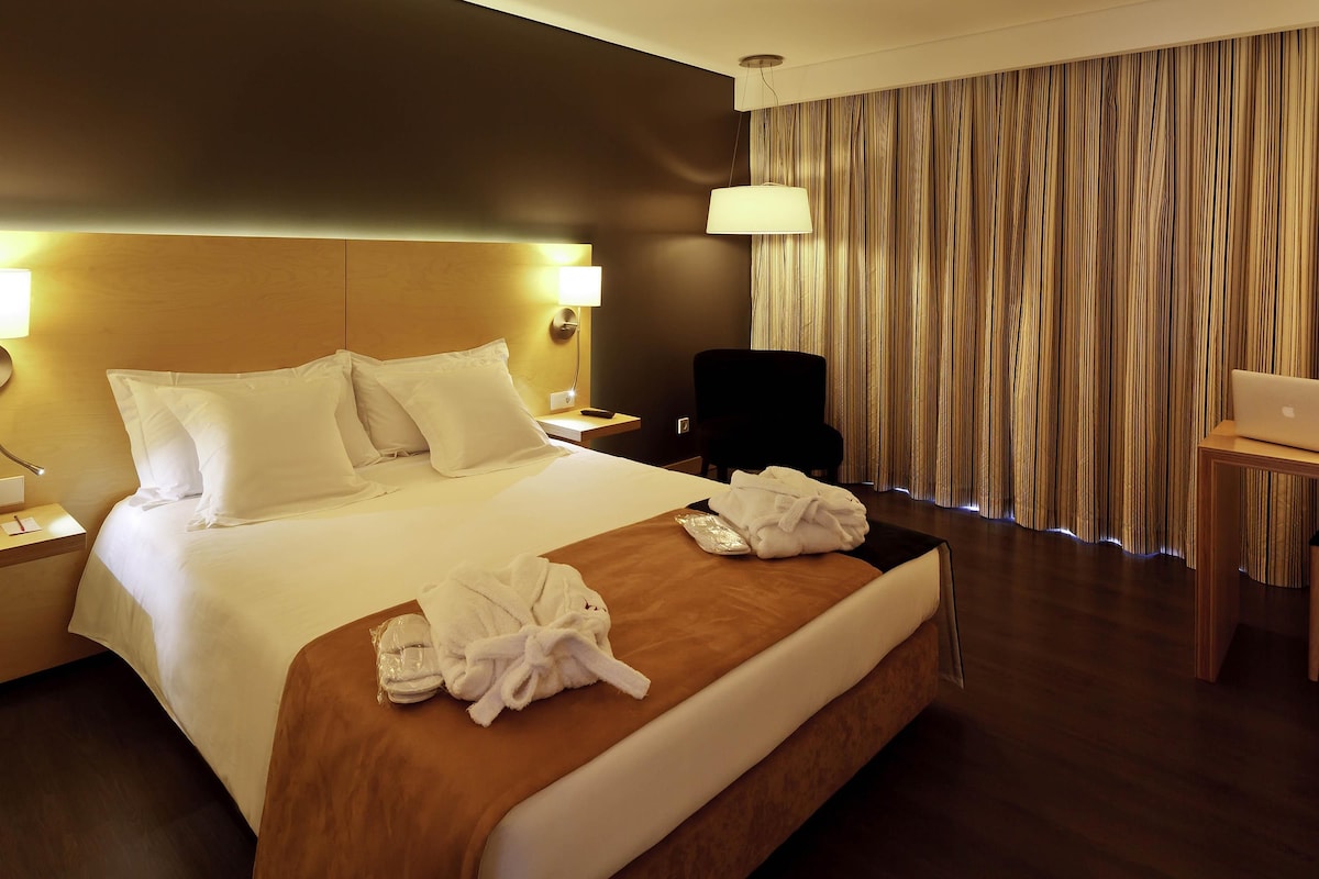A hotel room with a large bed, a desk, a chair, and a laptop.