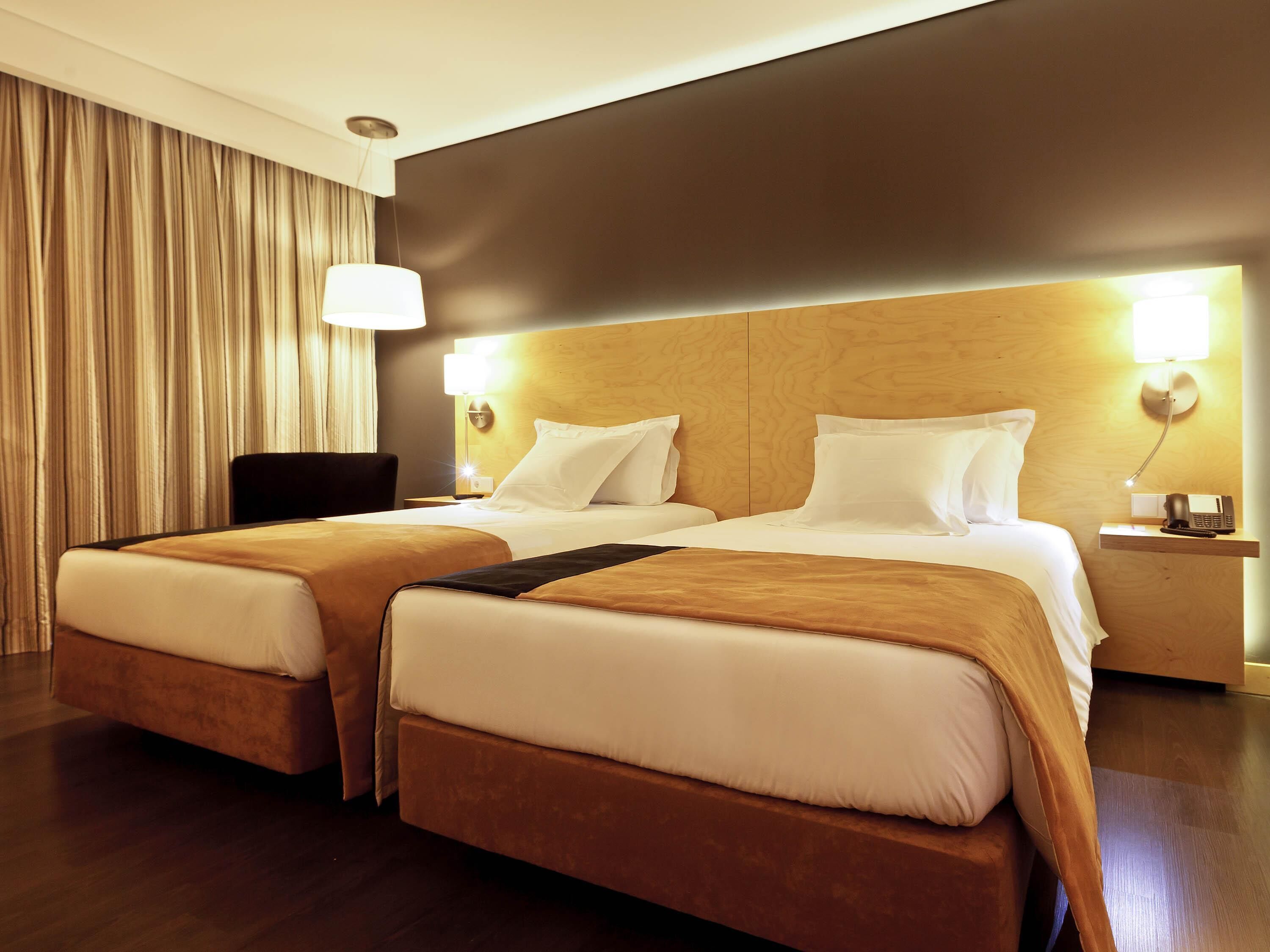 A hotel room with two beds, a chair, a desk with a phone, and a lamp.
