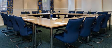 A conference room with a long table, blue chairs, and a carpeted floor.