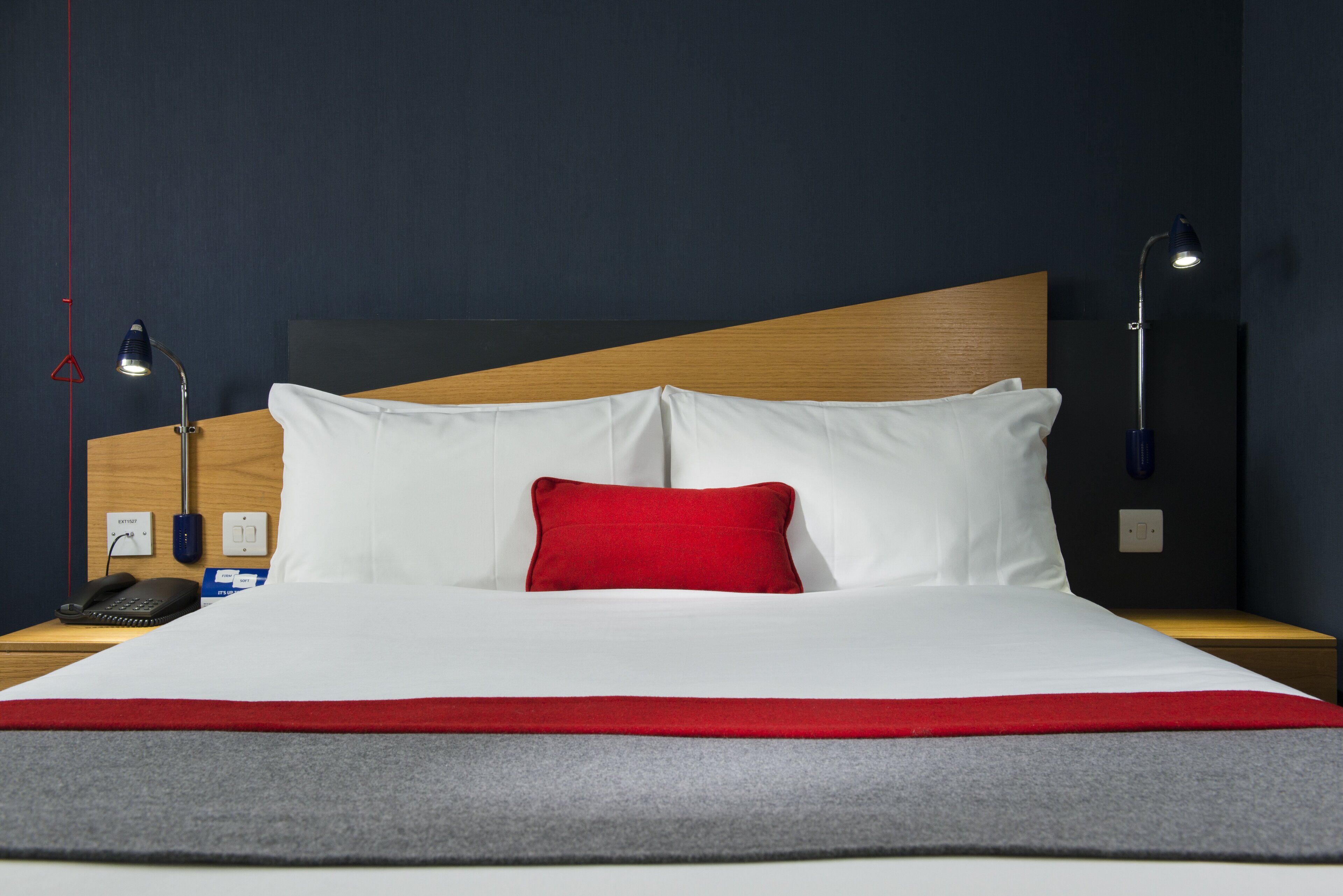 Ein Hotelzimmer mit einem großen Bett, zwei Nachttischlampen, einem Holz-Kopfteil und einem roten Kissen.