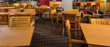 A restaurant with wooden tables and chairs, a patterned carpet, and a bar area with a red wall and a clock.