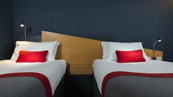 Two beds with wooden headboards, white bedding, and red pillows. Each bed has a bedside table with a lamp.