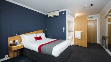 Una habitación de hotel con cama, mesita de noche y una puerta de madera que da a un baño.