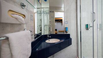 A modern bathroom with a glass-enclosed shower, a sink with a dark countertop, and a towel rack.